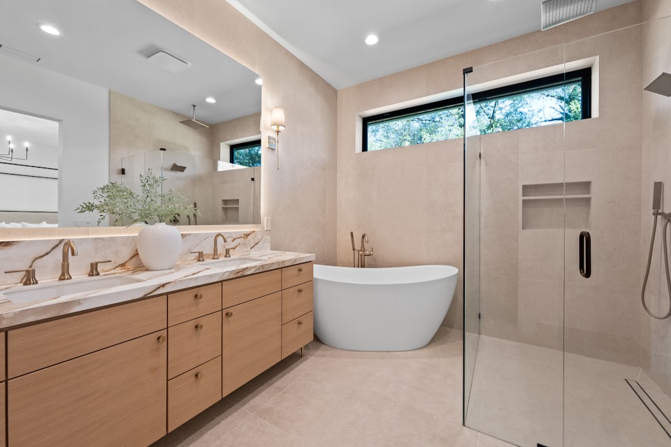 A warm modern bathroom with a glass walk-in shower and wood vanity